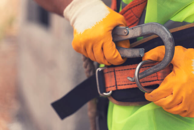 Construction worker clipping on harness safety belt to prevent construction accident fall