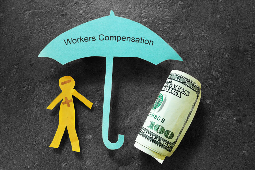 paper man cut out next to paper umbrella cut out stating workers compensation next to rolled-up hundred dollar bill