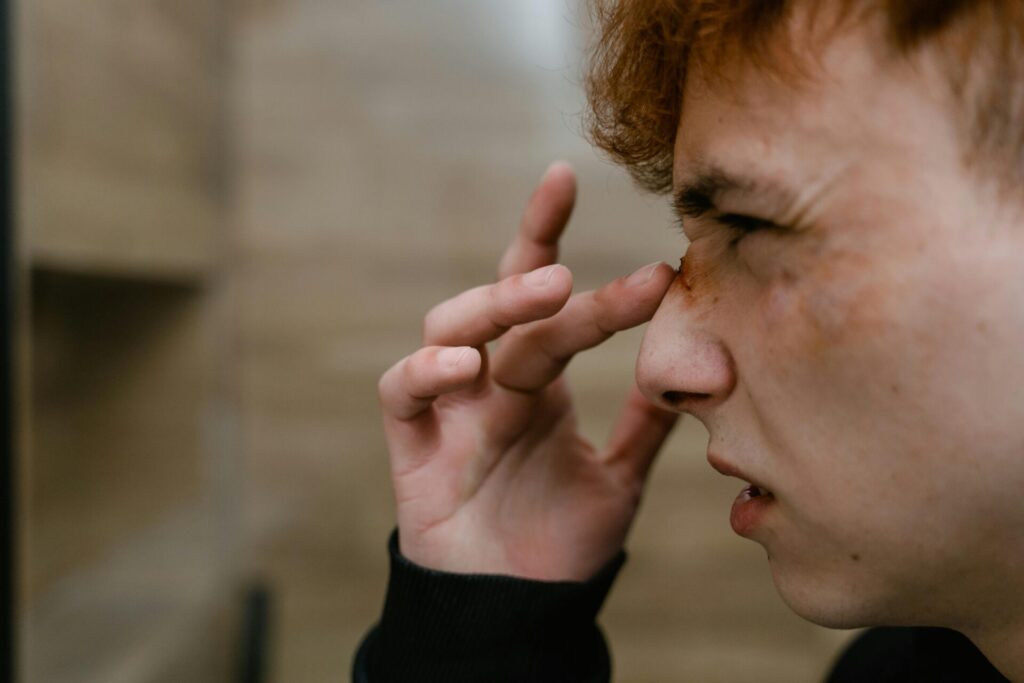 Close-up of a young man examining his facial injury in the mirror.